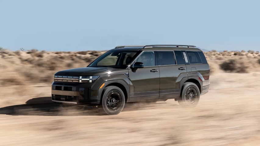 Dark-colored SUV driving through a desert landscape, kicking up dust at high speed under a clear blue sky.